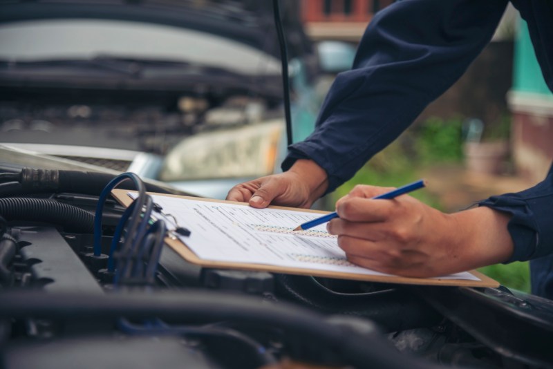 A mechanic performing a mobile pre-purchase car inspection in Seattle, checking a vehicle’s condition and filling a detailed inspection report.